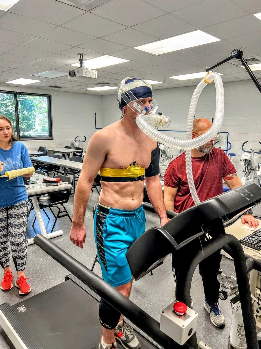 Thibault on a treadmill wearing a metabolic mask and chest sensors while two staff members monitor the test. Maximal treadmill exercise test with a metabolic cart and chest sensors.